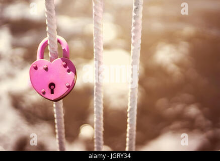 Pink Wedding closed lock in the form of heart. The castle weighs in at a bridge on a blue sky background. Retro style Stock Photo