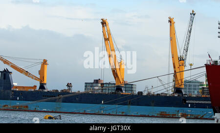 A large bulk carrier loaded with ship cranes. Ship in cargo port terminal. Container ship being unloaded in the Rotterdam harbor. Trade sea port . Stock Photo