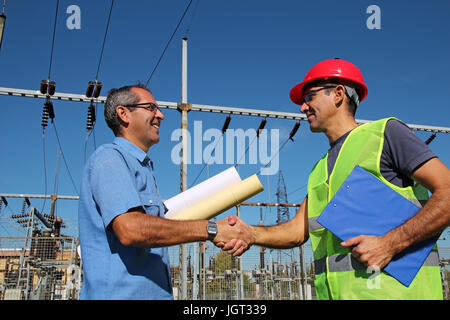 Smiling workers with blueprints and clipboard in meeting at electrical substation. Selective focus. Stock Photo