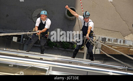Workers hanging on climbing ropes, showing raised fist sign.
