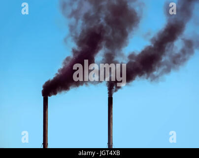 Two black Pipe which is thick black doom on a blue sky. Pollution of the environment. Stock Photo