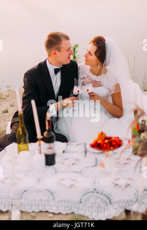 The side view of the happy newlyweds having the romantic picnic near the river. Stock Photo
