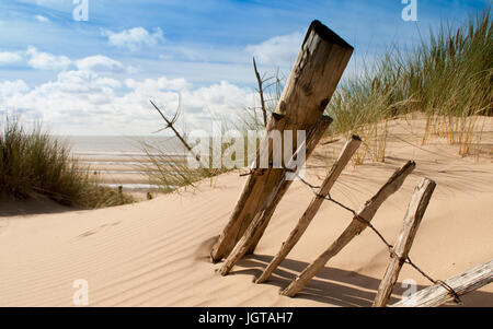 seascape view of a broken old fence remnants on a sand dune with sea in the background Stock Photo