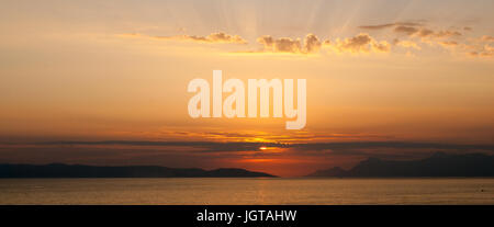 panoramic image of golden sunset with sun low above the sea and sunrays coming through clouds above Stock Photo