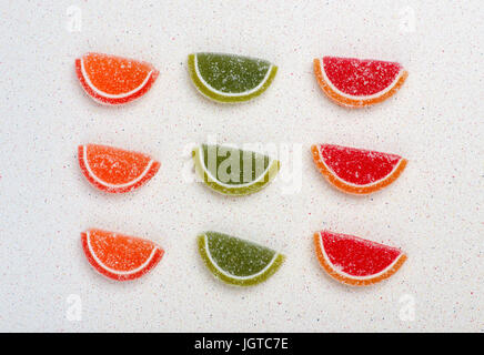 Fruit jelly in the form of citrus fruits are divided by color into three rows and three bars on a gray table top Stock Photo