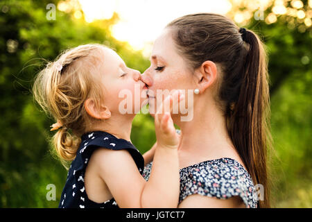 Young mother in nature holding little daughter in the arms. Stock Photo