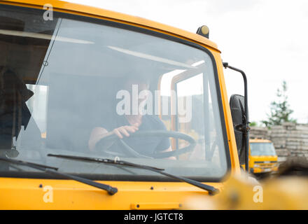 Male trucker in cabin of his yellow truck. Stock Photo