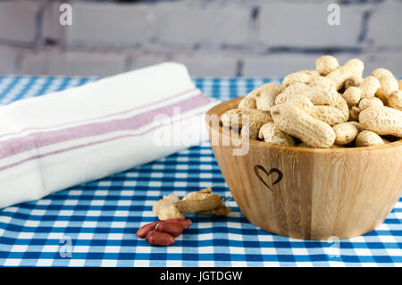 unshelled monkey nuts in a wooden bowl engraved with a heart shaped symbol Stock Photo