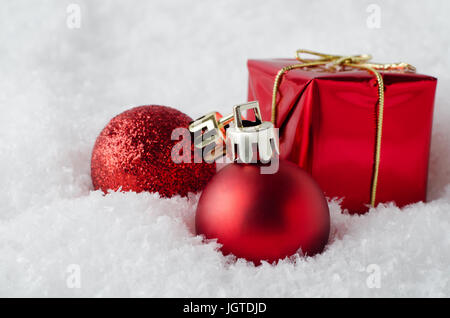 An arrangement of red Christmas decorations sinking into soft, white artificial snow.  Includes glitter and matte  baubles and gift box. Stock Photo