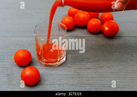 Freshly made tomato juice in a glass jug and in a mug on a wooden board. Stock Photo