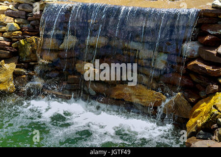 Waterfall at the source. Small Modern fountain in the park on the summer territory. A small fountain in the middle of a small artificial lake Stock Photo
