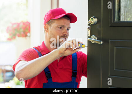 locksmith in red uniform installing new house door lock Stock Photo