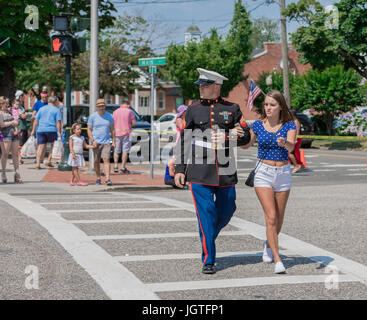 man in military uniform with woman crossing the street in Southampton, ny during a fourth of july parade Stock Photo
