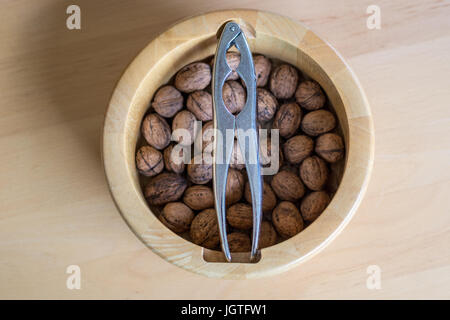 A bowl of walnuts with a nutcracker on a wooden table as seen from above Stock Photo