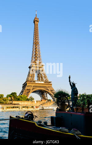The Eiffel tower in Paris, France, seen from the Debilly pier at sunset with a small Statue of Liberty, the river Seine and tourist shuttles. Stock Photo