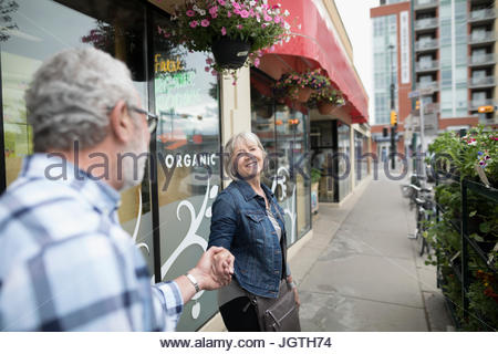 Affectionate senior couple holding hands, walking along storefront on urban sidewalk
