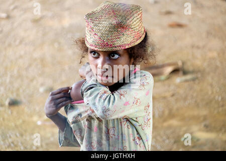 Young girl with old clothes at Mahabako station on the Fianarantsoa-Côte Est railway in Madagascar. She wears the traditional raffia hat of the region Stock Photo