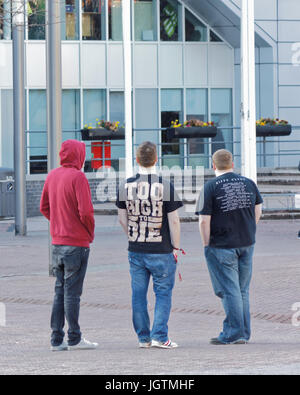 three young guys students teenagers boys viewed from behind in a cityscene setting 'too high to die tee shirt' hoody hoodie Stock Photo