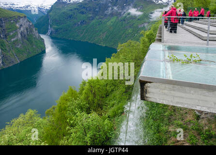 Artificial waterfall with tourists looking at view from high Eagles Road viewpoint platform overlooking Geirangerfjorden fjord. Geiranger Norway Stock Photo