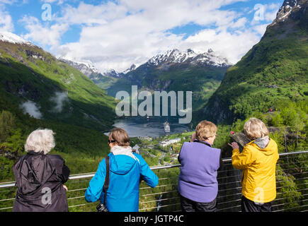 Four female tourists looking at scenic view from a viewpoint overlooking Geirangerfjorden fjord and village. Geiranger, Møre og Romsdal county, Norway Stock Photo