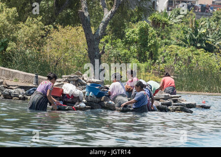 Several women of mixed ages in the typical native dress cleaning and washing clothes, Lake Atitlan,  Guatemala Stock Photo