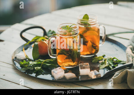 Summer refreshing cold peach ice tea with fresh mint in glass jars on metal tray over wooden garden table, selective focus Stock Photo