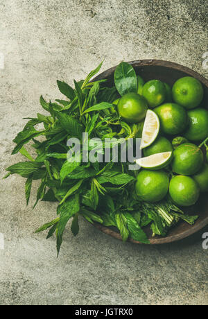 Flatlay of freshly picked organic limes and mint leaves for making cocktail or lemonade in wooden plate over grey concrete stone background, top view, Stock Photo