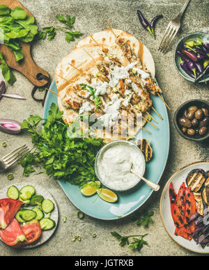 Summer barbecue party dinner set. Flatlay of grilled chicken skewers with yogurt dip, flatbreads, fresh parsley, vegetables, marinated olives and chil Stock Photo