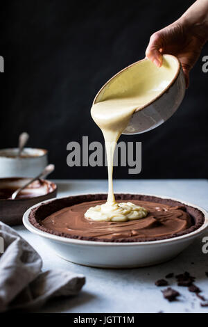 A chocolate pie base being filled with melted chocolate Stock Photo