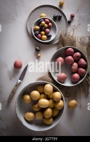 Different kinds of mini potatoes in a ceramic bowl on a marble table on top view Stock Photo