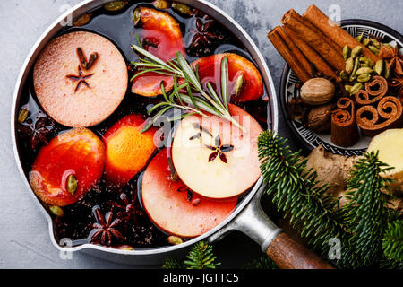 Mulled wine hot drink with citrus, apple and spices in aluminum casserole on concrete background close-up Stock Photo