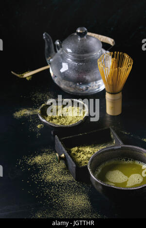 Green tea matcha powder and hot drink in black bowls and wood box standing with glass teapot, bamboo traditional tools spoon, whisk in terracotta tray Stock Photo