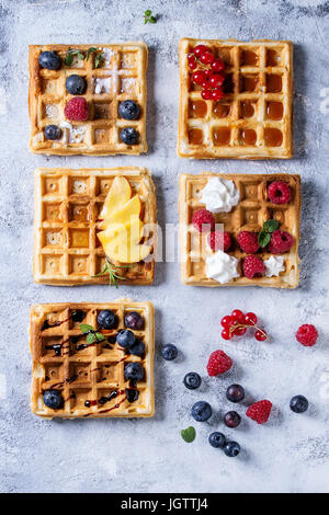 Homemade square belgian waffles with fresh ripe berries blueberry, raspberry, red currant, peach served with caramel, balsamic sauce, honey, whipped c Stock Photo