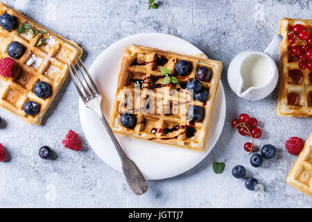 Homemade square belgian waffles with fresh ripe berries blueberry, raspberry, red currant, peach served with caramel, balsamic sauce, honey, whipped c Stock Photo