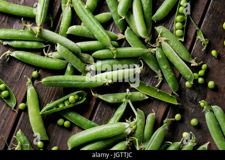 Young organic green pea pods and peas over old dark wooden planks background. Top view with space. Harvest, healthy eating. Stock Photo