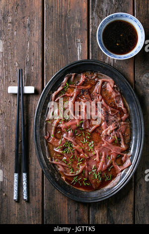 Asian style Beef carpaccio with soy sauce, chive onion, black sesame, served on vintage metal tray with bowl of sauce and chopsticks over old wooden p Stock Photo