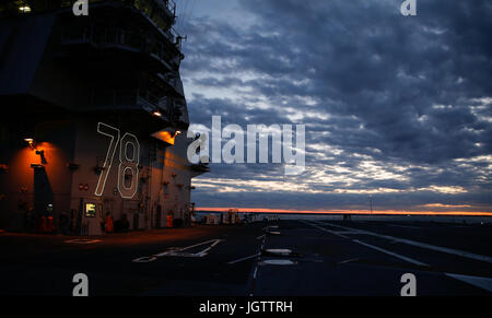 The exterior flight deck lights of Pre-Commissioning Unit Gerald R. Ford (CVN 78) illuminated during sunset to maintain visibility aboard the aircraft carrier through the night until morning colors. Stock Photo