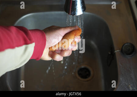 Male hand with sponge and running over a metal sink needs to be clean, selective focus artificial light photo Stock Photo
