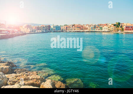 view of sun rising over mountains and lighting old part of Chania with rocks at foreground, Crete Stock Photo