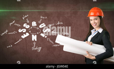 Woman in orange helmet near wall with blueprints and business idea sketch drawn on it. Concept of a successful business. Stock Photo