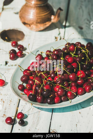 Plate of sweet cherries on light blue wooden table background
