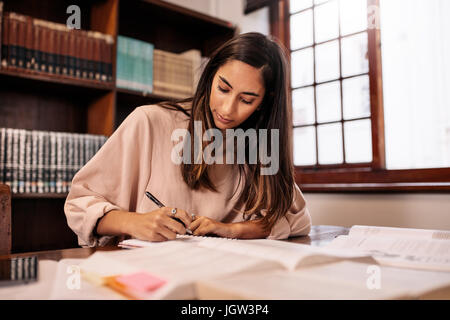 Young student making notes in the library. College female student preparing for the exam while sitting in library. Stock Photo