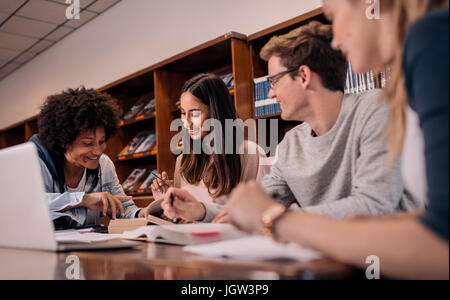 Young people sitting at table reading reference books for study notes. Group of young students doing assignment in library. Stock Photo