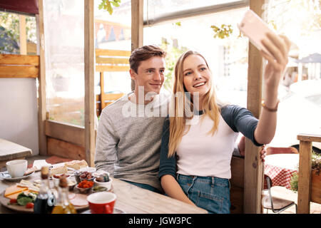 Couple taking photos of themselves with mobile phone in cafe. Stylish young couple catching memories by smart phone. Stock Photo