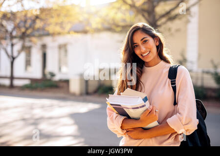 Beautiful young woman with backpack and books outdoors. College student carrying lots of books in college campus. Stock Photo