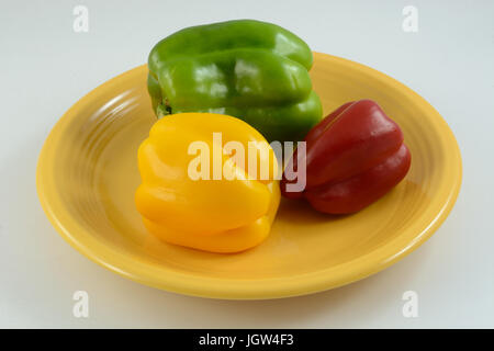 Yellow, red and green whole raw bell peppers on yellow plate on white wooden table Stock Photo