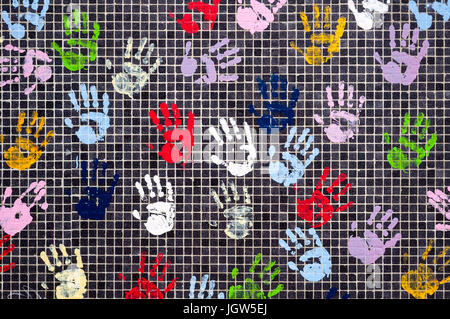 Many multicolored children handprints with finger paint on a black tiled wall. Stock Photo