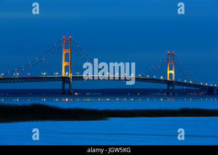 Mackinac Bridge at night. Its lights twinkle and create reflections on winter ice. Stock Photo