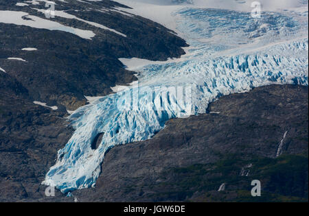 The blue ice of a glacier slides down a rocky mountain side in south central Alaska. Stock Photo