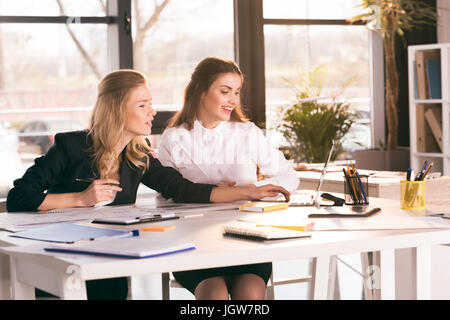 Two professional young businesswomen sitting at table and using laptop Stock Photo